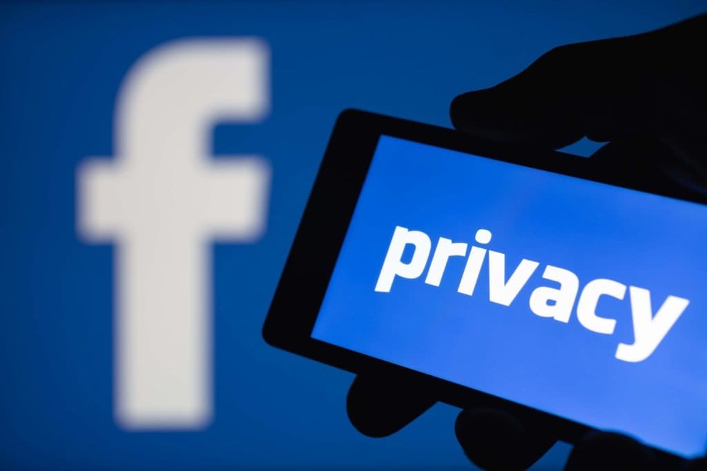 The Facebook logo in the background with a phone in front of it with "Privacy" on the screen