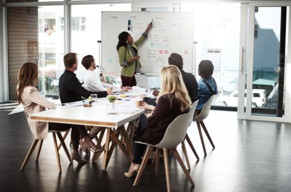 A group of people in a meeting room with marketing plans on a whiteboard