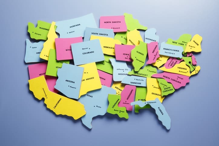 Puzzle pieces representing the fifty states of the United States are jumbled and slightly misplaced on a blue background.