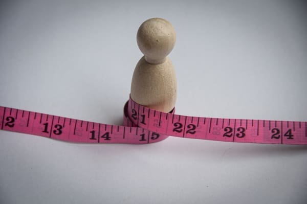 A wooden figure with a measuring tape around it