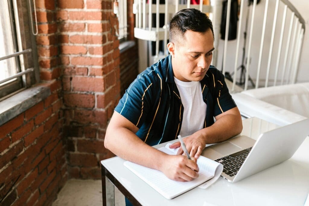 Young man studying with a laptop and notebook at a modern home interior.